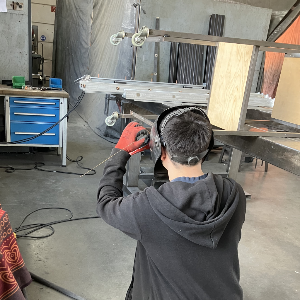 Mann repariert ein hohes Regal mit Schweißgerät in einer Werkstatt - unkomplizierte Hilfe