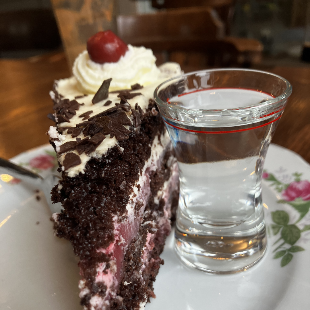 Ein Stück Schwarzwälder Kirschtorte auf einem Teller, daneben ein kleines Glas Kirschschnaps – hier Symbol für menschliche Dienstleistung und echte Begegnung.