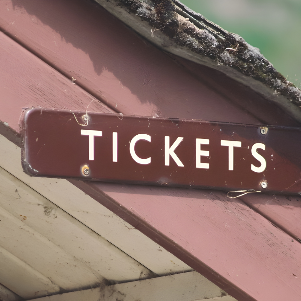 Ein braunes Schild mit der weißen Aufschrift "Tickets" ist an einem Hausdach befestigt und weist auf Eintrittskarten hin.